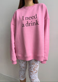 Person wearing a pink sweatshirt with 'I need a drink' text and white lace pants.
